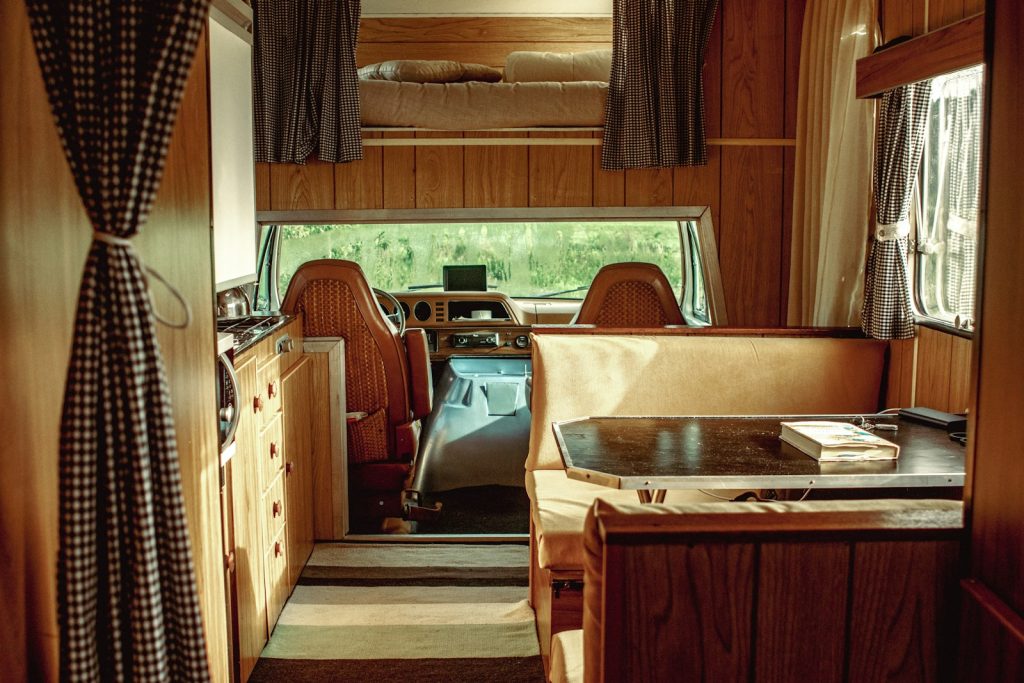 the inside of a camper with a desk and chairs. an illustrative image to depict the effect of changing window treatments in an rv camper. changing the aesthetic can be helped by knowing how to remove an rv valance. 